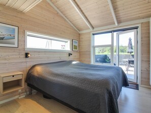 A bedroom with a large bed, wooden walls, a window, and a small bedside table.