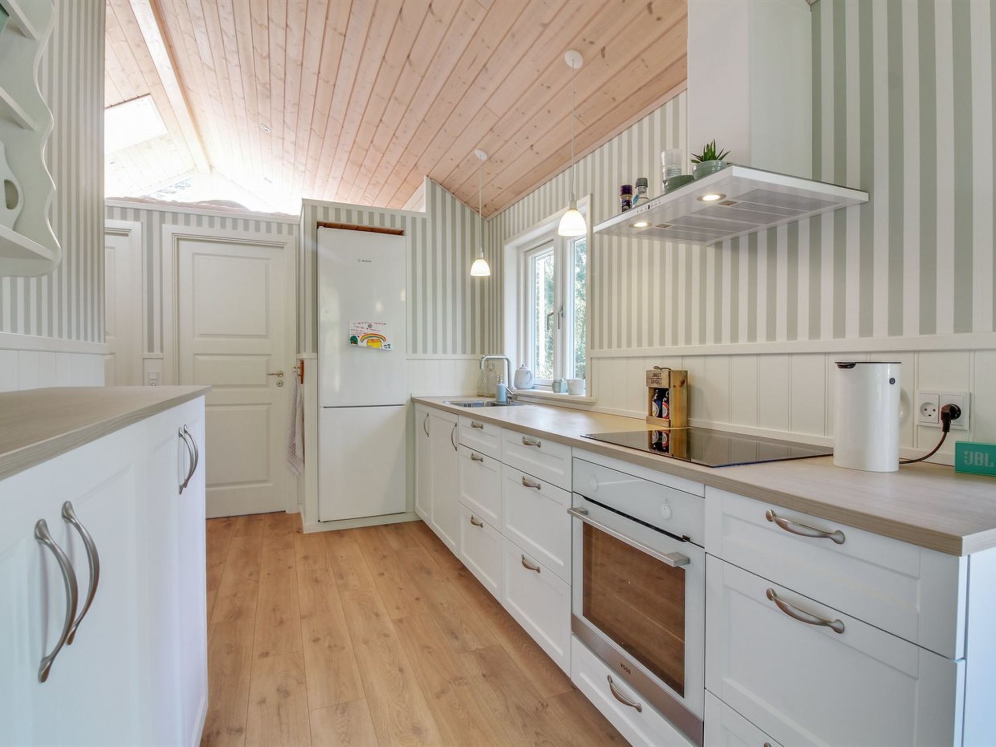 A modern kitchen with white cabinetry, a wooden countertop, a built-in oven, and a window providing natural light.