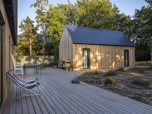 Une terrasse en bois avec des meubles d’extérieur, un petit bâtiment doté d’un toit en métal et un décor naturel composé d’arbres.