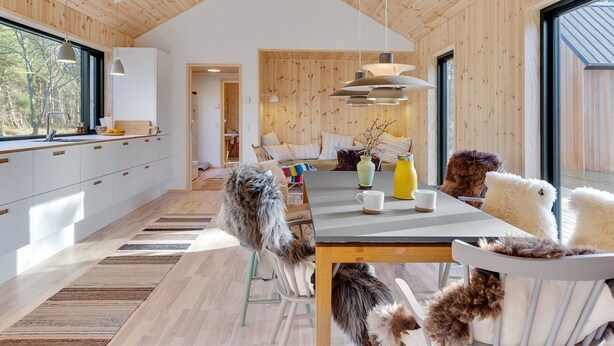 Un intérieur moderne avec des murs lambrés, une grande table à manger au centre et une vue dégagée grâce à de larges fenêtres.