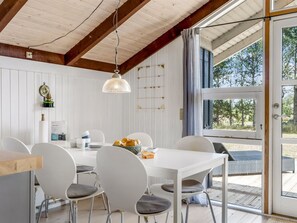 A dining area with a white table and chairs, a hanging light fixture, and a view through a glass door.
