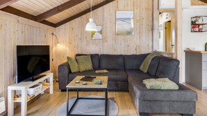 Un salon chaleureux avec un grand canapé d’angle gris, un téléviseur à écran plat et un plafond en bois.