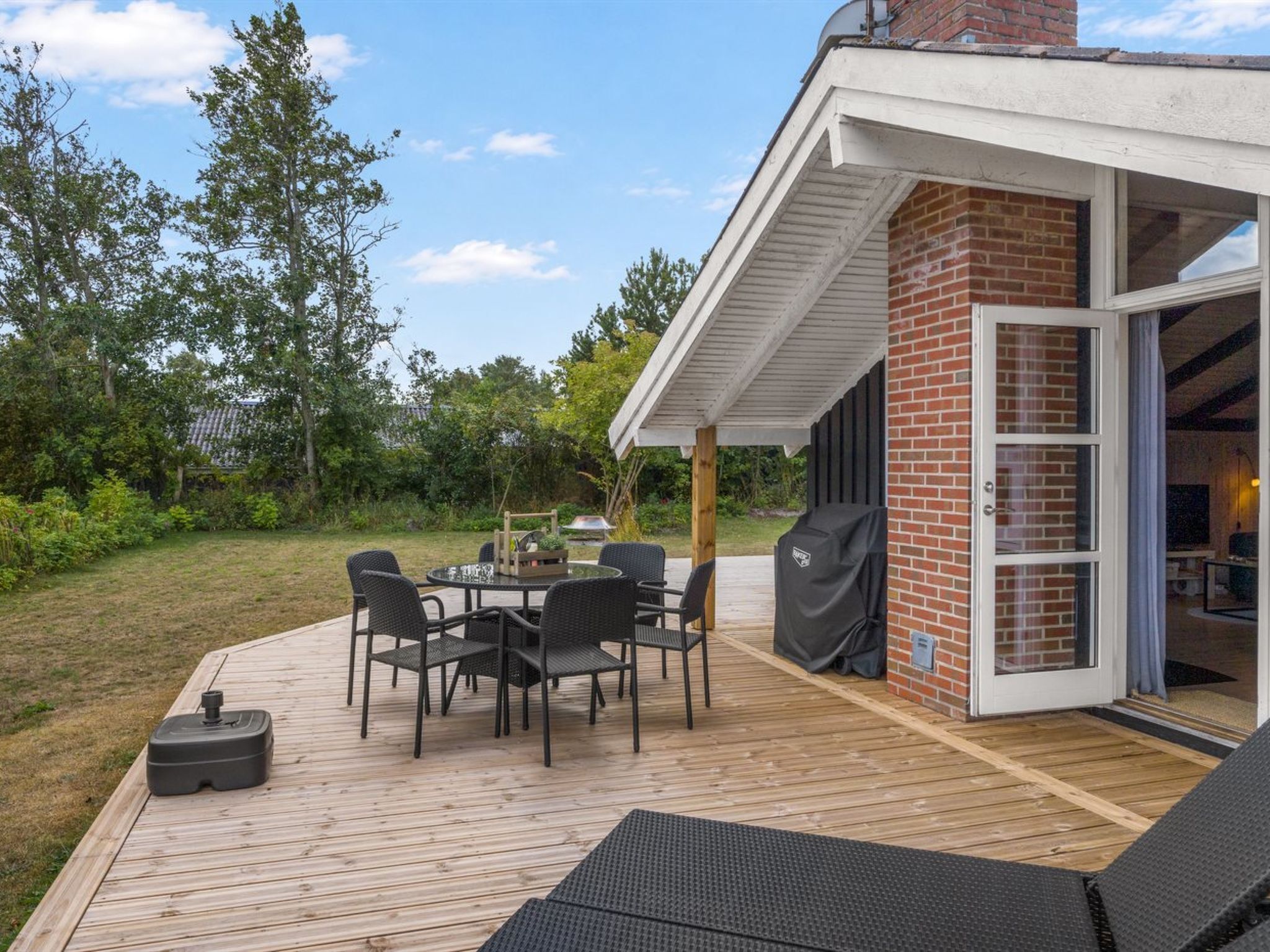 A deck with outdoor furniture, a grill, and a brick wall with a sliding glass door.