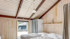 A bedroom with a wooden ceiling, a bed with white bedding, a window with curtains, and a shelf with decorative items. - "Eliana" - 350m from the sea by Interhome (Strandby)