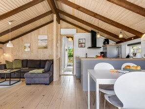 Ein gemütliches Interieur mit Holzbalkendecke, einer Couch, einem Esstisch und einer Küchenzeile.