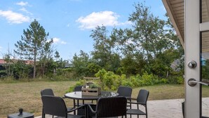 Une terrasse extérieure avec une table ronde et quatre chaises, entourée d’une plateforme en bois et d’une zone herbeuse avec des arbres.