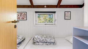 Une pièce avec une porte en bois, une fenêtre donnant sur des arbres et deux lits avec une literie à motifs floraux.