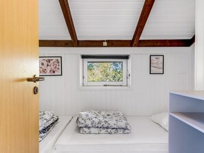 A room with a wooden door, a window with a view of trees, and two beds with floral bedding.
