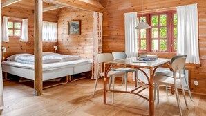 A cozy cabin with a wooden interior, a bed, a dining table with chairs, and a window with curtains.