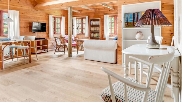 A cozy wooden cabin interior with a dining area, a living room, and a TV mounted on the wall.