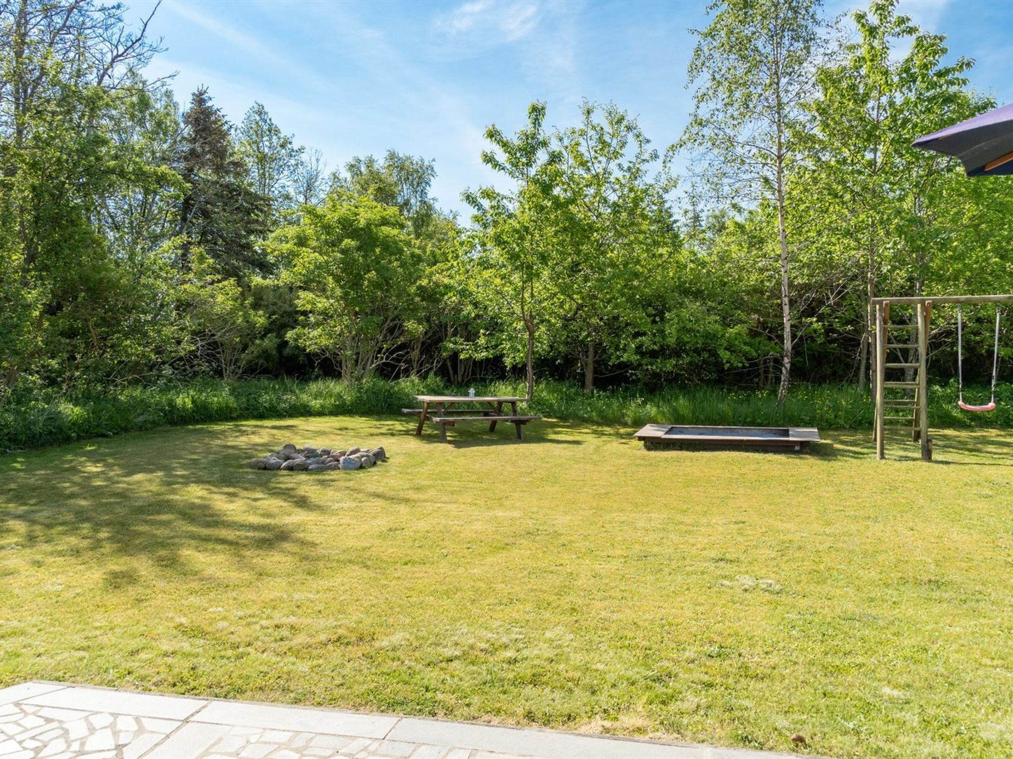 A grassy outdoor area with a picnic table, a bench, and a swing set.