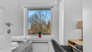 A modern bedroom with a bed, a desk, and a chair. There is a window with a view of trees and a clear sky. - "Ehm" - 600m from the sea by Interhome (Strandby)