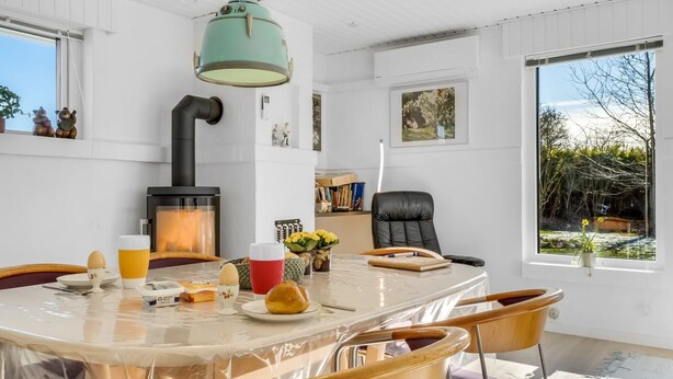 A modern kitchen with a wood-burning stove, a dining table with chairs, and a large window with a view of trees. - "Ehm" - 600m from the sea by Interhome (Strandby)