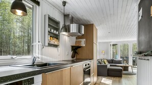 Una cocina moderna con un ventanal grande, armarios de madera, horno empotrado y comedor con sofá y mesa.