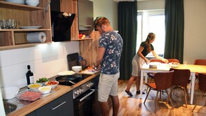 A modern kitchen with wooden cabinets, a built-in oven, and a dining area with a table and chairs. - Sankt Anna Resort (Sankt Anna)