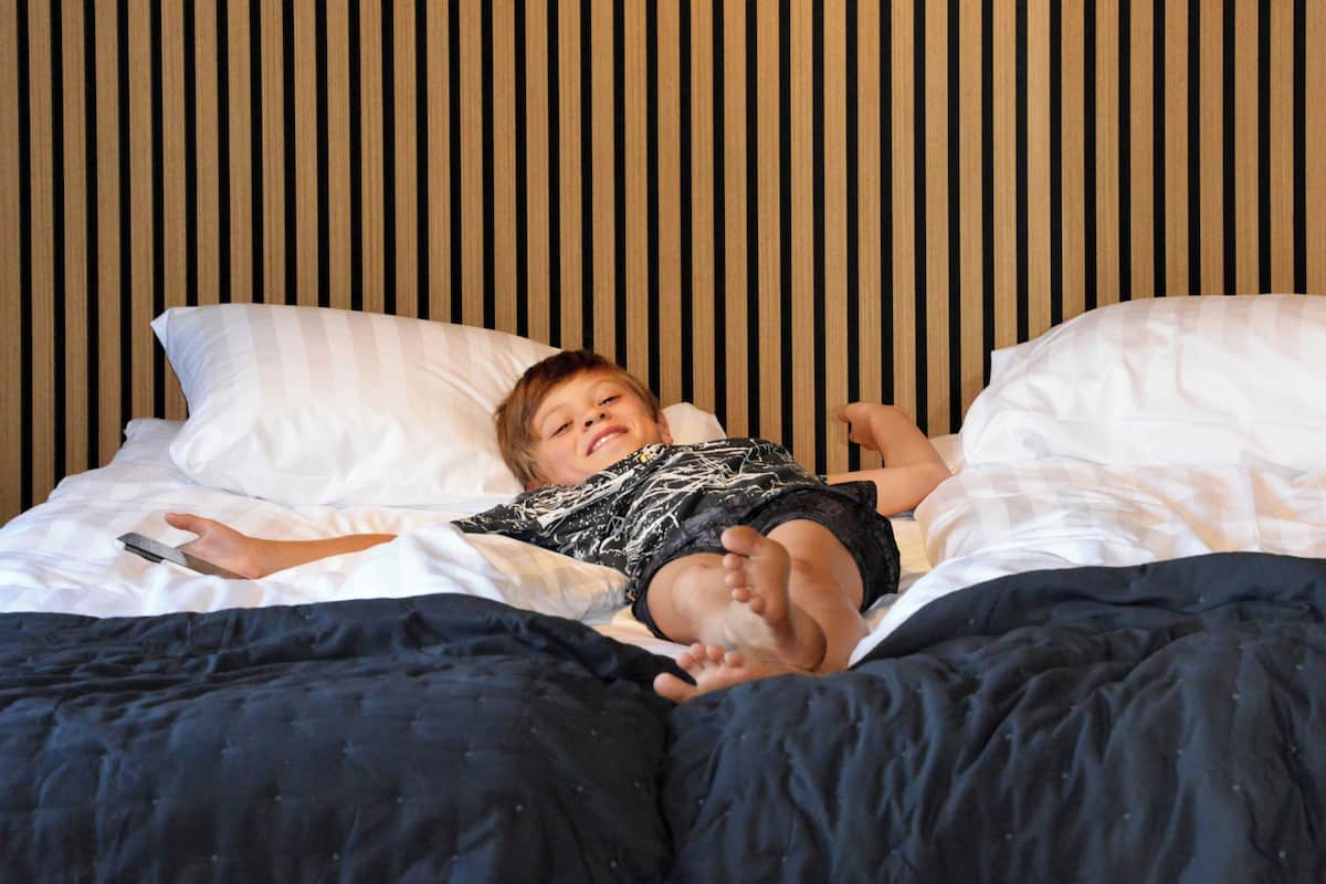 Ein Kind liegt auf einem Bett mit weißen Kissen und einer dunkelblauen Decke.