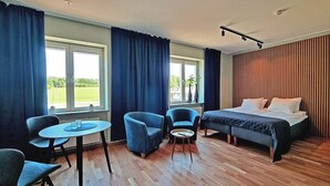 A modern hotel room with a bed, two blue armchairs, a small round table, and a view of the outdoors. - Sankt Anna Resort (Sankt Anna)