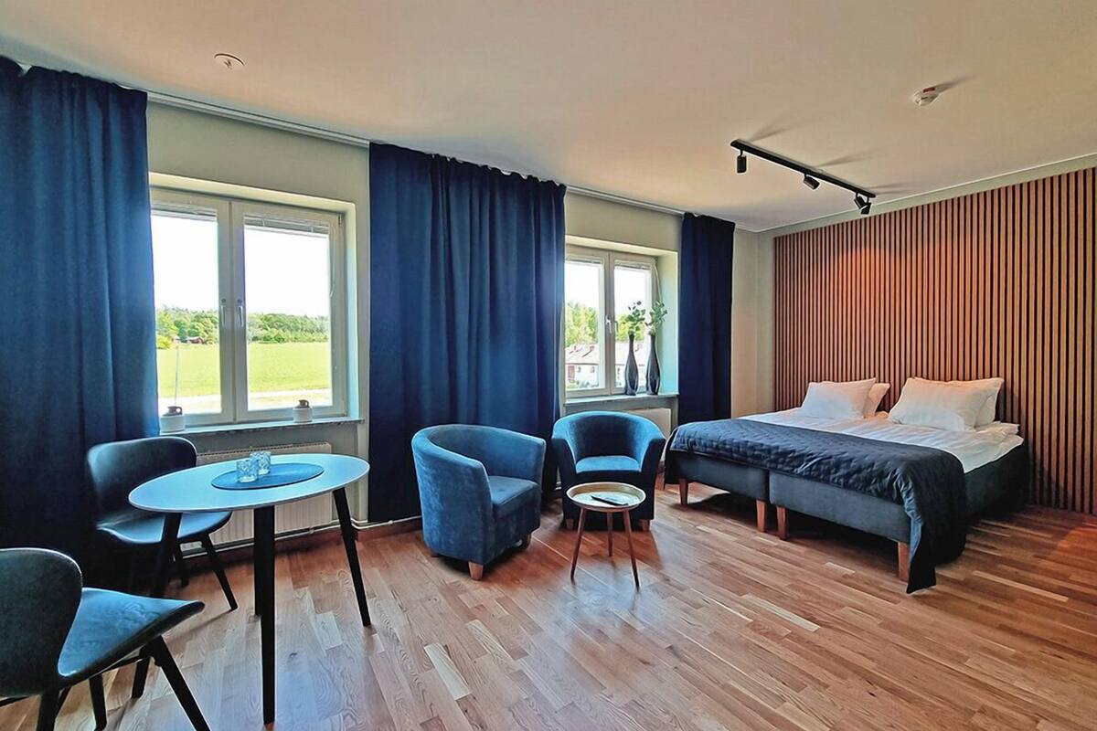 Ein modernes Hotelzimmer mit einem Bett, zwei blauen Sesseln, einem kleinen runden Tisch und Blick ins Freie.