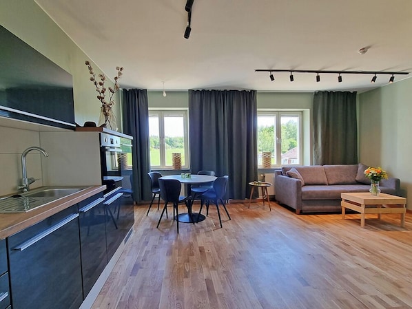 A modern kitchen with a dining area, a sofa, and a small table with a vase of flowers. - Sankt Anna Resort (Sankt Anna)