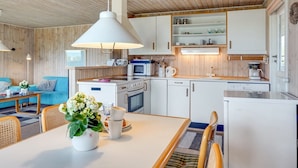 A modern kitchen with white cabinets, a microwave, a coffee maker, and a sink. There is a dining area with a table, chairs, and a vase of flowers.