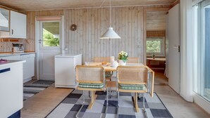A compact kitchen with wooden walls, a dining area with a table and chairs, and a large window providing natural light.