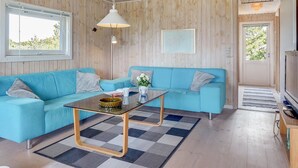 A modern living room with a blue sofa, a glass coffee table, and a wooden ceiling.