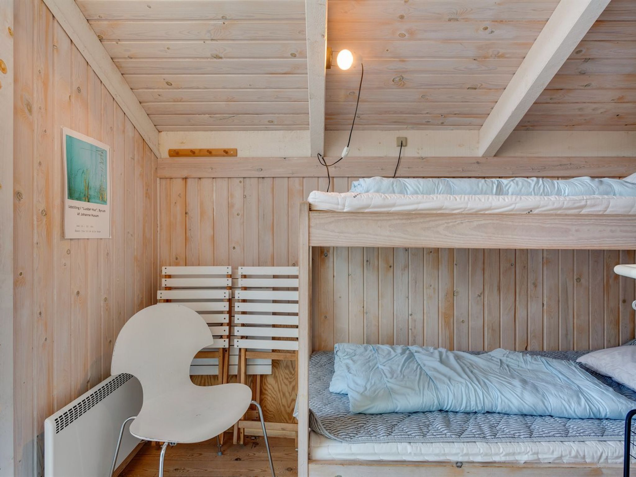 A wooden room with bunk beds, a white chair, and a wall-mounted light fixture.