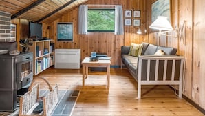 L’intérieur d’un chalet accueillant, avec un plafond en bois, un canapé, une télévision, une cheminée et une bibliothèque.