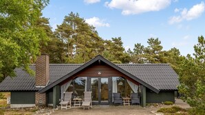 Une cabane dotée d’une grande porte vitrée, d’une cheminée en briques et d’un espace extérieur aménagé pour s’asseoir.