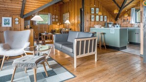 L’intérieur de ce chalet accueillant est doté de murs en bois et d’un plafond haut. On y trouve un coin repas avec une table et des chaises, un canapé et un coin cuisine avec un comptoir et des tabourets.