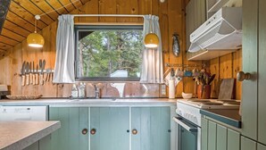 Une cuisine avec des meubles de rangement en bois, une fenêtre avec des rideaux et des ustensiles de cuisine suspendus.