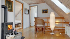 A cozy attic room with a wood-burning stove, a wicker chair, and a sloped ceiling.