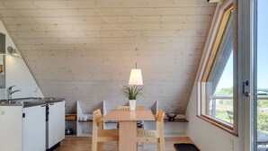 A compact kitchen with a wooden table and chairs, a small potted plant, and a window with a view of the outdoors.
