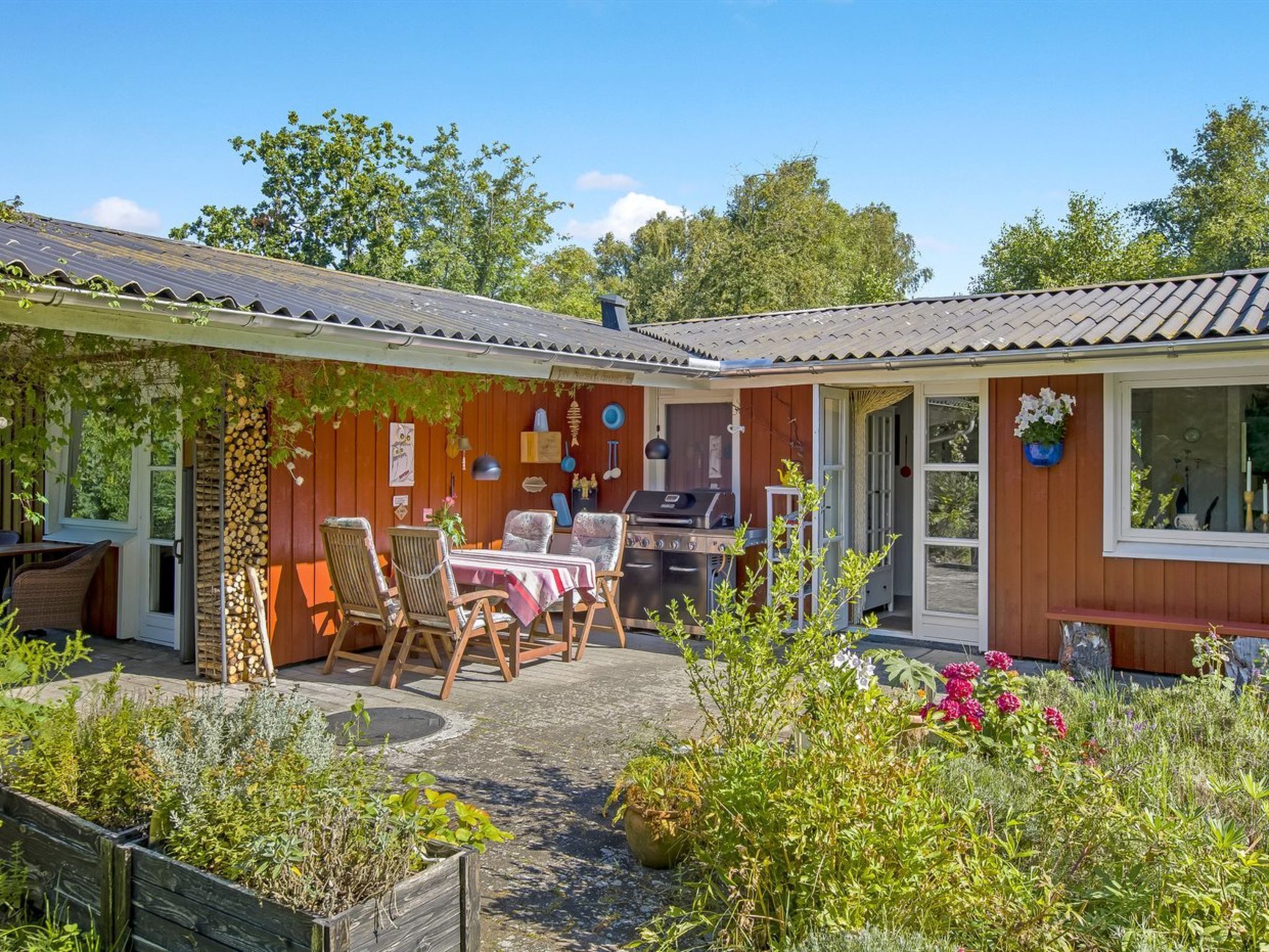 Een houten huis met terras, tuinmeubels en een barbecue.