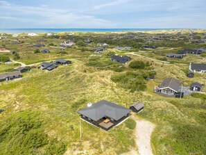 Vista aérea de una zona residencial con casas, un espacio abierto amplio y un sendero que lleva a un edificio con techo oscuro.