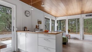A modern kitchen with white cabinetry, a wooden countertop, and a large window overlooking a forest.