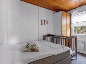 Een kamer met een bed, een ledikant, een kledingkast en een raam met uitzicht op bomen.