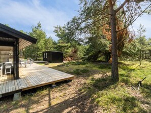 Een houten terras met buitenmeubels, een klein huisje en een bebost gebied.