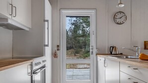 A modern kitchen with white cabinetry, a wooden countertop, a built-in oven, a sink, and a clock on the wall.