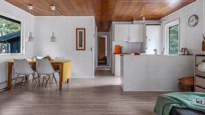 A modern kitchen with white cabinets, a wooden ceiling, and a dining area with a table and chairs.