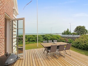 Une terrasse avec une table et des chaises, un barbecue et une vue sur la mer.