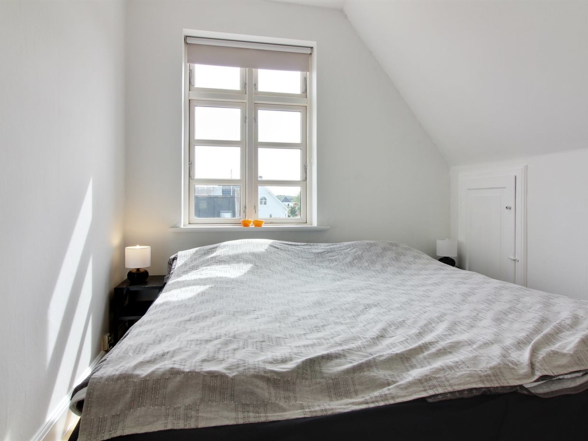 A bedroom with a large window, a bed, a nightstand, and a door.