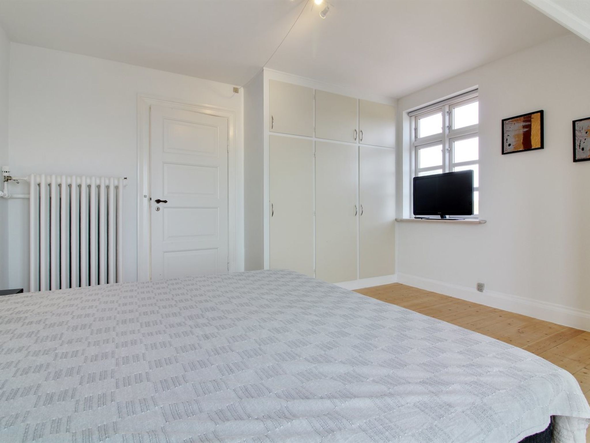 A bedroom with a bed, a radiator, a wardrobe, and a television on a wall.