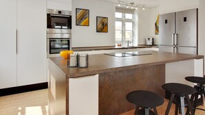 A modern kitchen with white cabinetry, stainless steel appliances, a large island with stools, and artwork on the walls. - "Kosara" - 50m from the sea by Interhome (Frederikshavn)