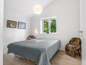 Ein Schlafzimmer mit einem Bett, einem Fenster, einer Lampe und zwei gerahmten Bildern an der Wand.