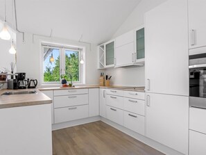 Eine moderne Küche mit weißen Schränken, einer Holz Arbeitsplatte und einem Fenster mit Blick auf Grünflächen.