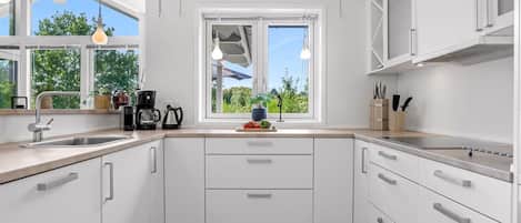 Une cuisine moderne avec des meubles blancs, un plan de travail en bois, un évier et une fenêtre donnant sur un espace verdoyant.