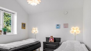 A bedroom with two beds, a window with a view of greenery, a teddy bear on a nightstand, and wall-mounted flower-shaped lights.