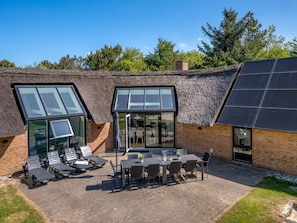 Ein modernes Gebäude mit einem Strohdach, großen Fenstern und einer Solaranlage.