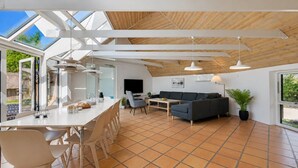 Ein geräumiger Wohnbereich mit hoher Decke, einem Esstisch mit Stühlen, einer Couch und einem Fernseher.